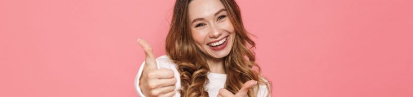 a woman dressed in white smiling with both hands thumbs up