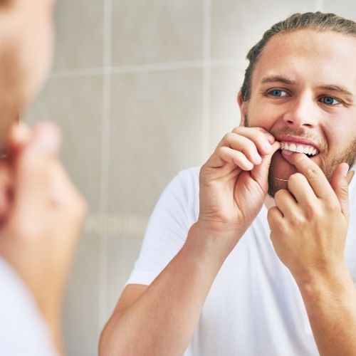 A man looking in the mirror while flossing.