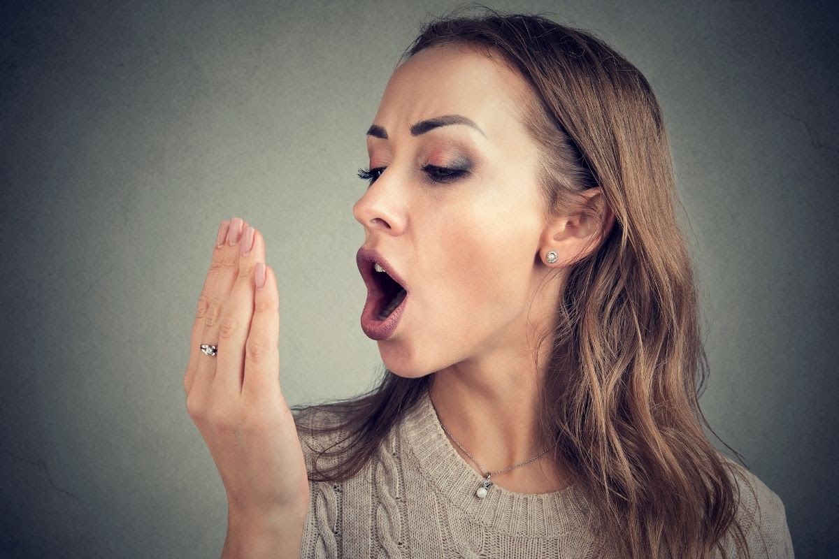 A woman smelling her breath after using dental probiotics.