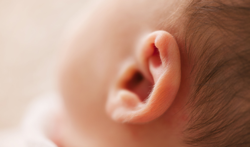 A baby is tugging on his ear because of having earwax.