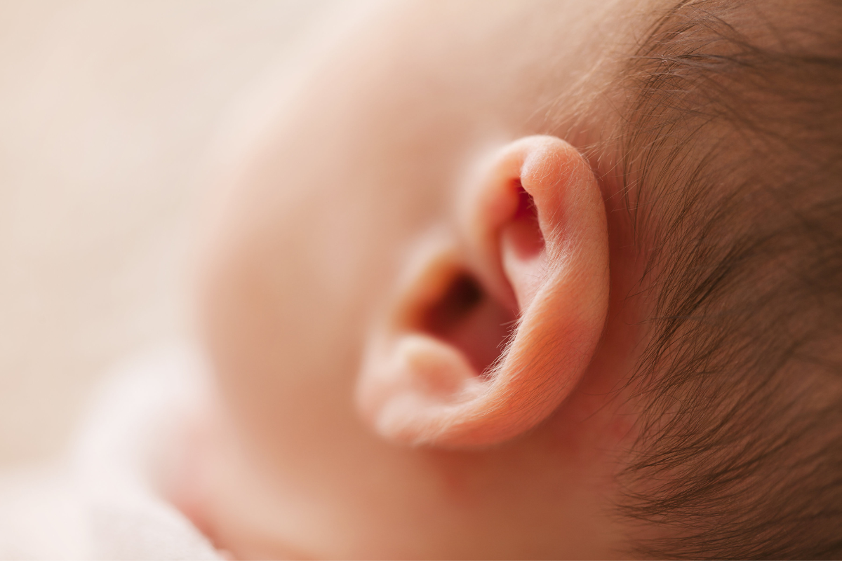 A baby is tugging on his ear because of having earwax.