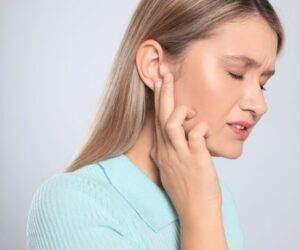 Close-up side profile of a woman gently pressing her fingers to her ear and jawline, face showing discomfort from pressure or pain, illustrating the typical symptoms of trapped fluid that lead people to search for methods on how to drain ear sinus fluid