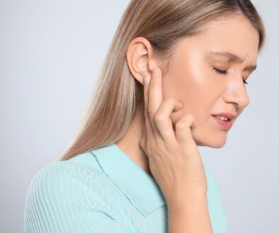 Close-up side profile of a woman gently pressing her fingers to her ear and jawline, face showing discomfort from pressure or pain, illustrating the typical symptoms of trapped fluid that lead people to search for methods on how to drain ear sinus fluid