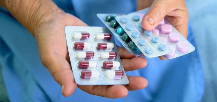 Hands holding various antibiotic pills, highlighting the link between antibiotic use and constipation after antibiotics.
