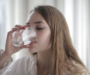 The woman is drinking water to prevent dehydration.