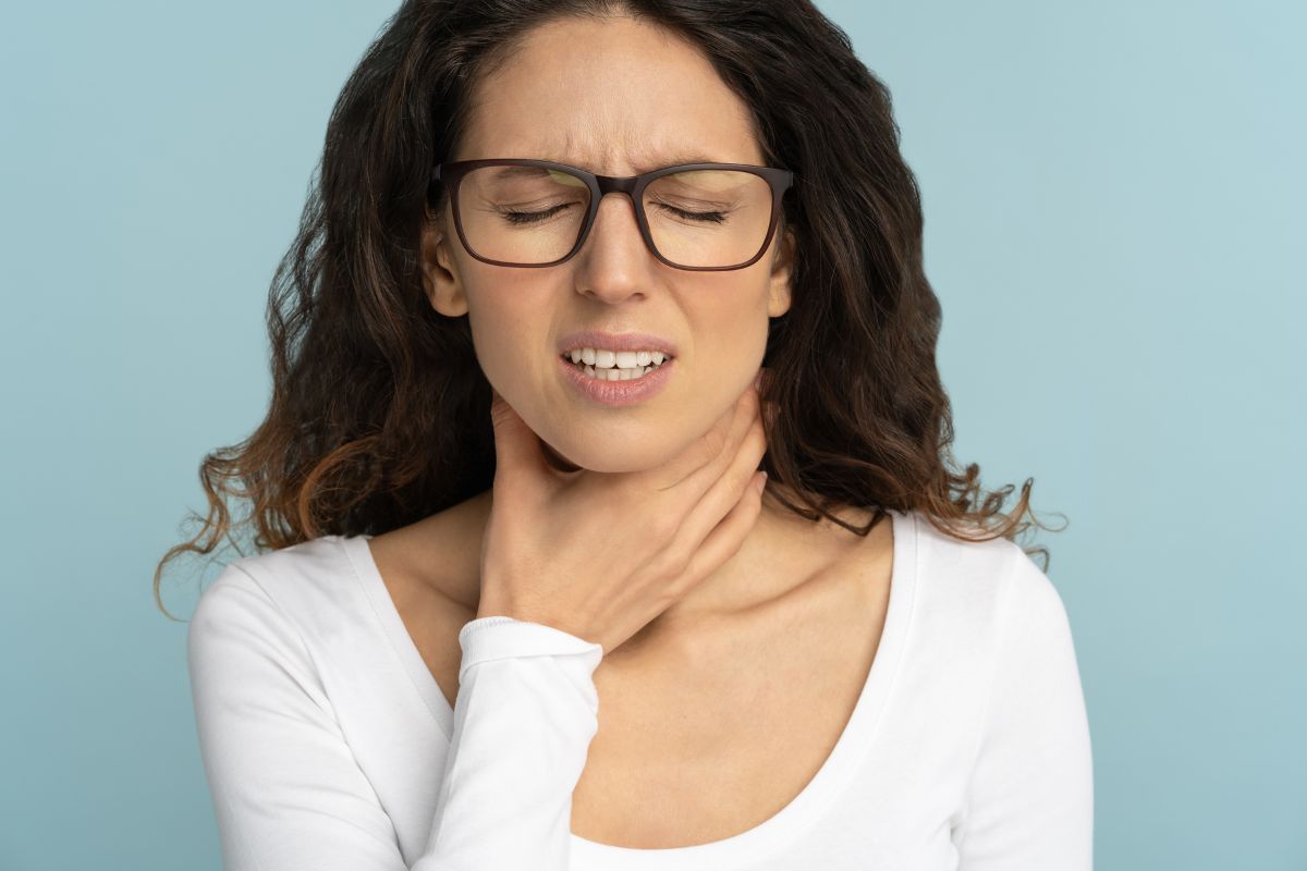 A person with tonsil stones, holding their throat.