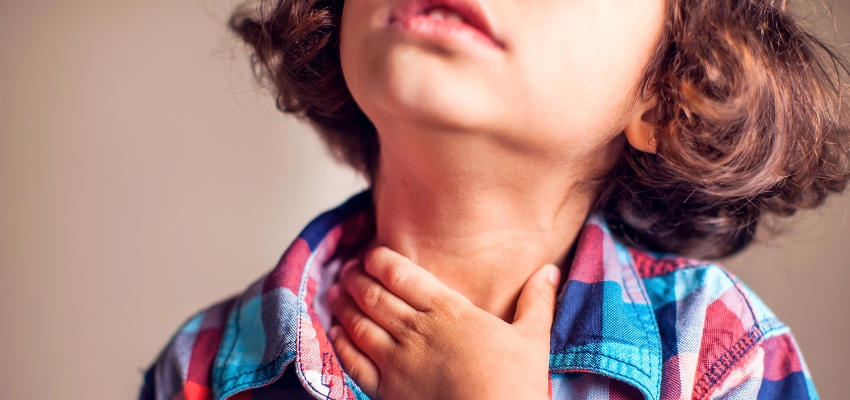 Young child holding their throat in discomfort, a common sign that may need post nasal drip child treatment.