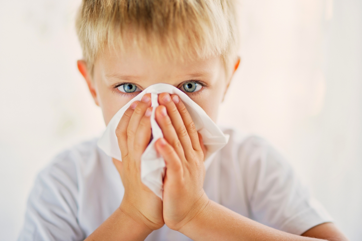Young boy blowing his nose into a tissue, illustrating symptoms addressed by post nasal drip child treatment.