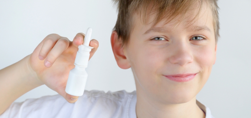 Smiling child holding a nasal spray bottle, a helpful option for post nasal drip child treatment.