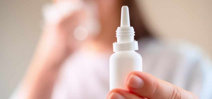 Person holding nasal spray bottle for treating crackling sound in sinuses