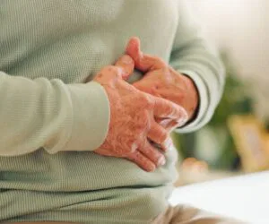 Elderly person holding their stomach in discomfort, representing the need for gut healing supplements.