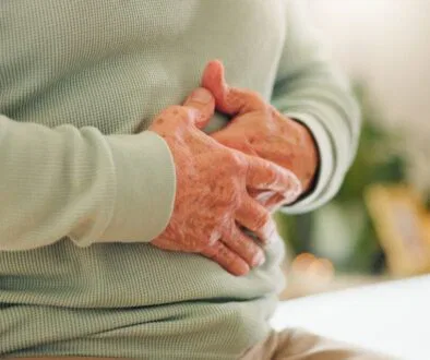 Elderly person holding their stomach in discomfort, representing the need for gut healing supplements.