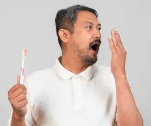 Man checking his breath with a toothbrush in hand, wondering why his breath smells after brushing.