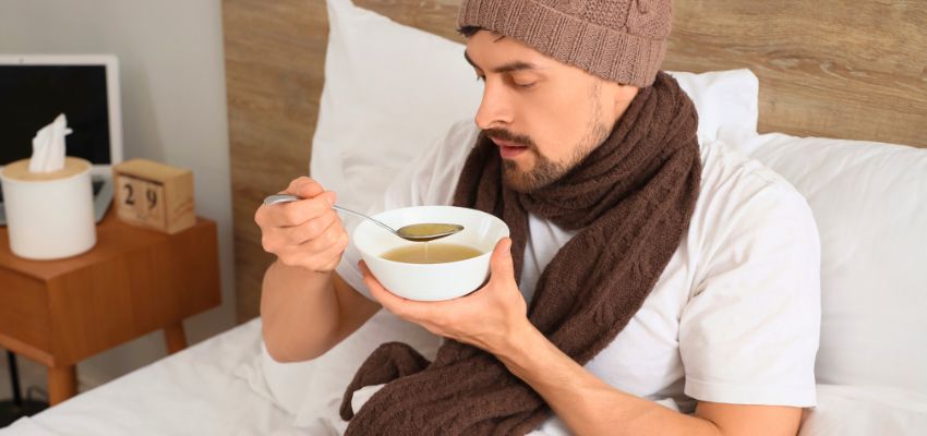 The man drinks hot broth and soup to relieve a sore throat.