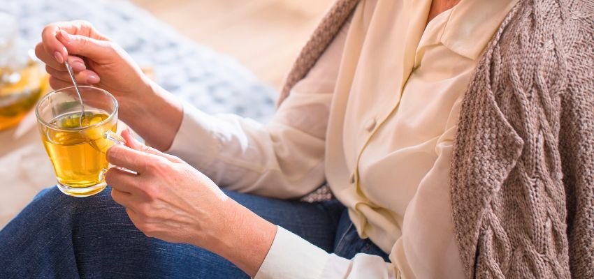 The woman drinks tea to relieve a sore throat.