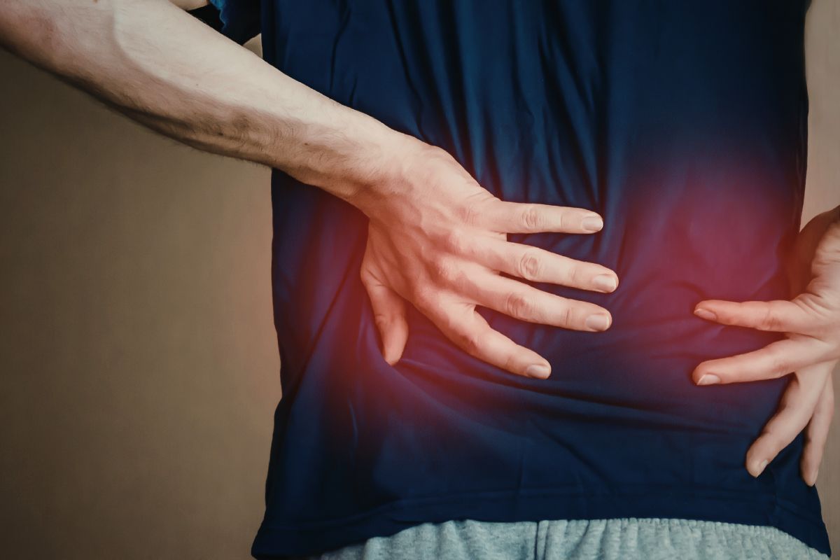 Side view of a man in a dark blue t-shirt standing and placing both hands on his lower and mid-back with a red glow highlighting the area of pain, conveying referred or radiating discomfort that prompts many to ask 'can gerd cause back pain' during episodes of severe reflux
