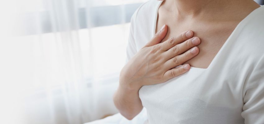 Close-up of a woman gently pressing her open hand against her upper chest near the sternum, illustrating the burning or pressing sensation in the chest commonly linked to acid reflux and raising the question 'can gerd cause back pain' as referred discomfort