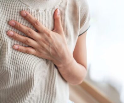 Close-up of a woman’s hand gently pressing against her chest, conveying the burning or pressing sensation in the chest and upper abdomen typical during a GERD flare up