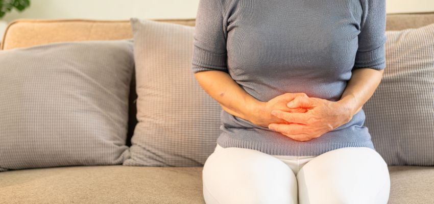 A person sits on a couch clutching their stomach with a highlighted area of discomfort, highlighting the need for IBS friendly foods.