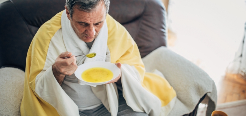 Man wrapped in a blanket enjoying warm soup, one of the best foods that clear sinus congestion.