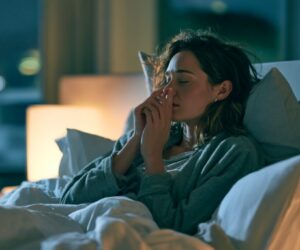 Woman in bed holding her nose, struggling with nasal congestion at night.