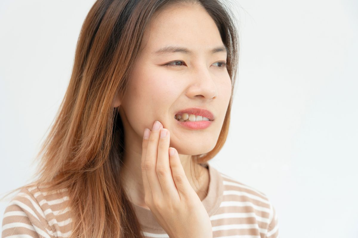 Woman holding her jaw in discomfort while noticing what does gingivitis smell like.