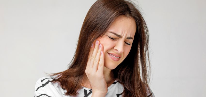 Woman holding her cheek in discomfort after surgery, a common concern with bad breath after tooth extraction.