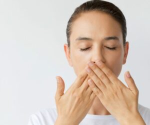 Woman covering her mouth while worried about bad breath after tooth extraction.
