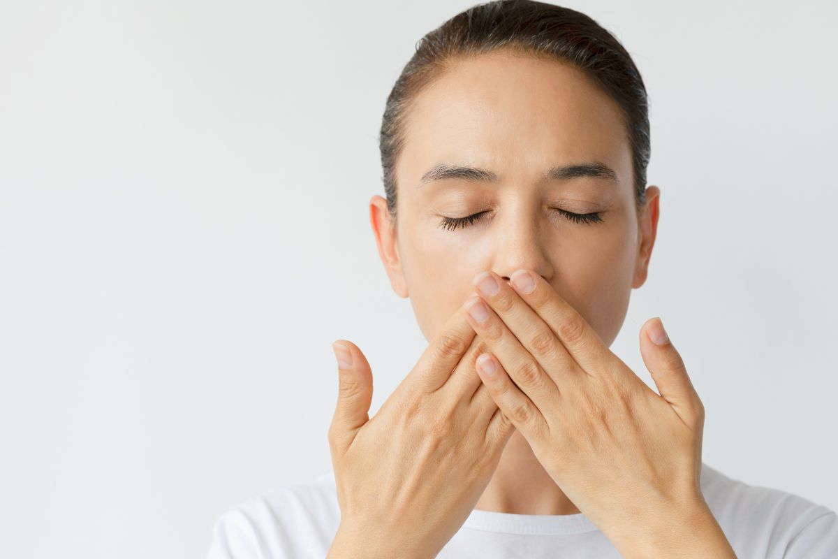 Woman covering her mouth while worried about bad breath after tooth extraction.
